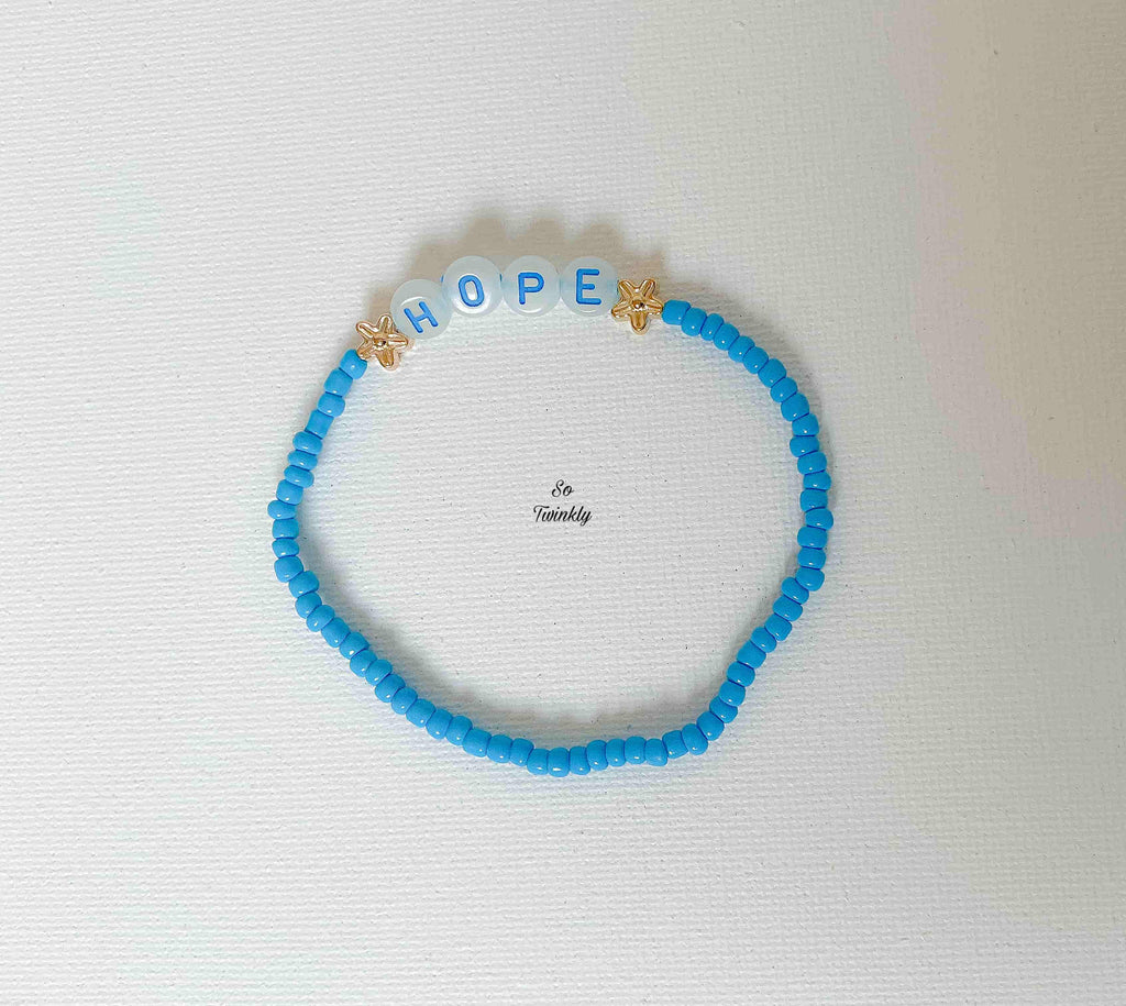 Flat lay of handmade Hope bracelet featuring soft blue pearls and a minimalist charm that inspires positivity