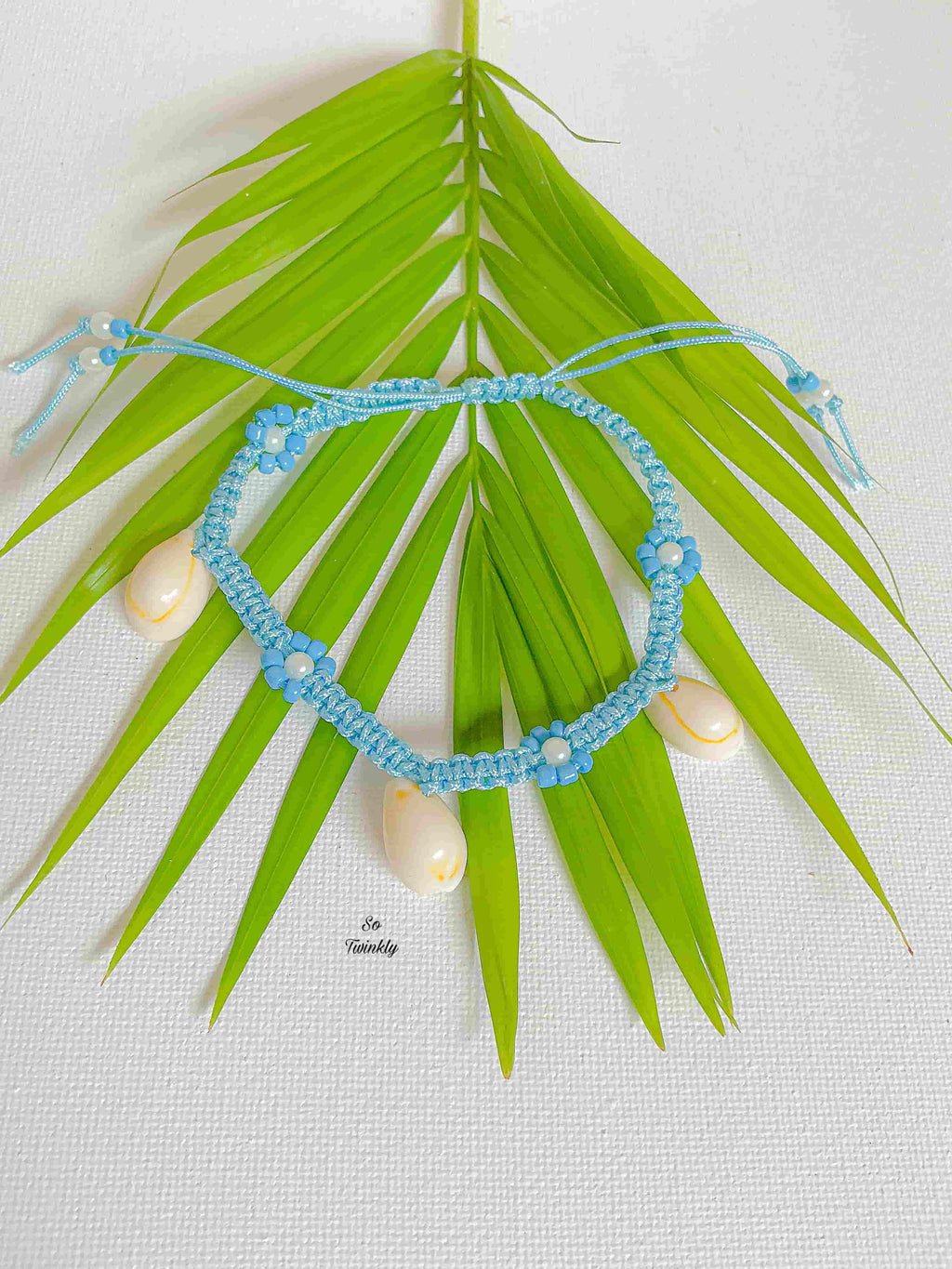 Flat lay of adjustable seashell anklet with blue cord, white and blue acrylic pearls, and natural shells