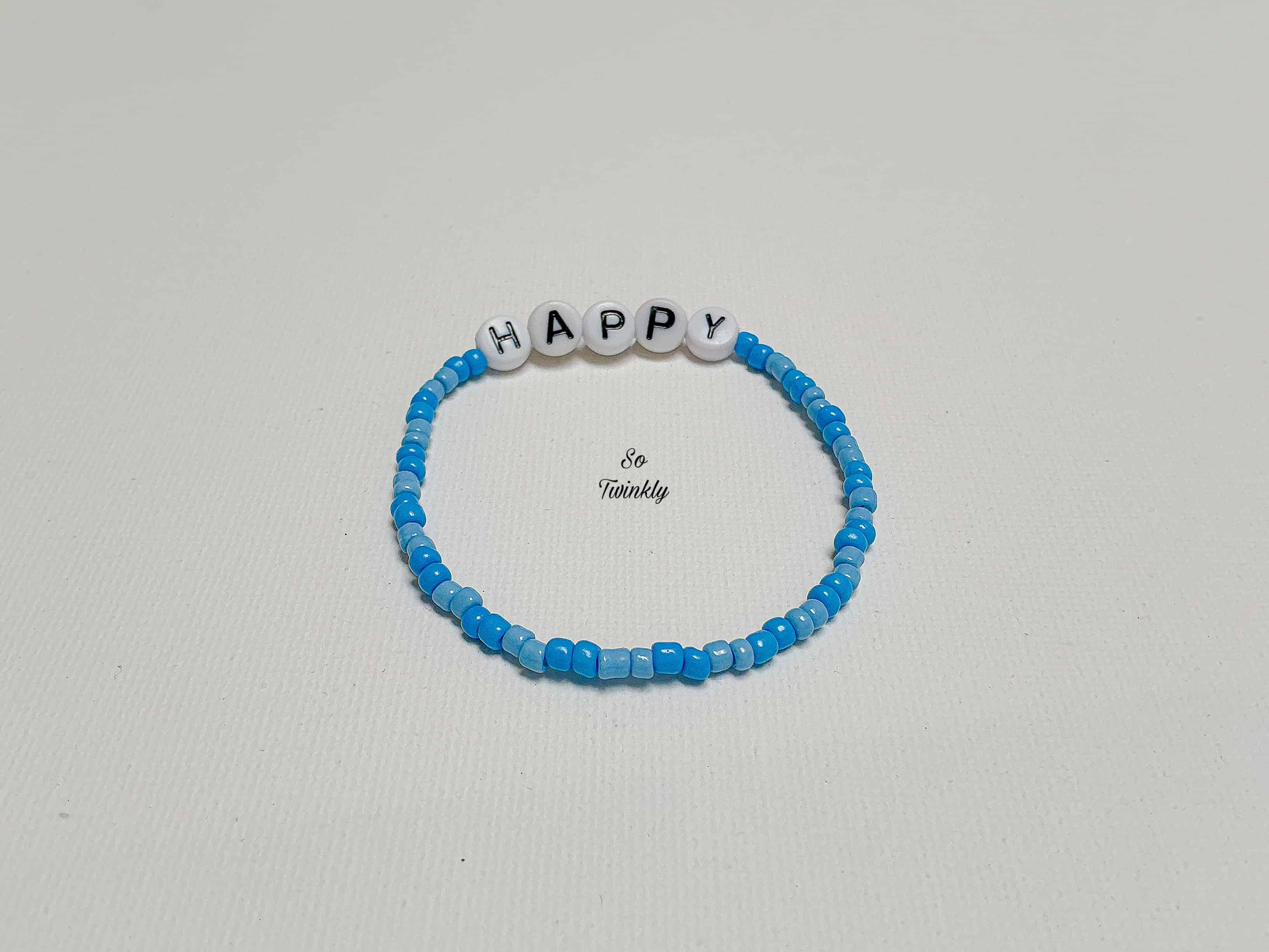 Flat lay of handmade Happy bracelet with soft and deep blue acrylic beads arranged in a subtle gradie