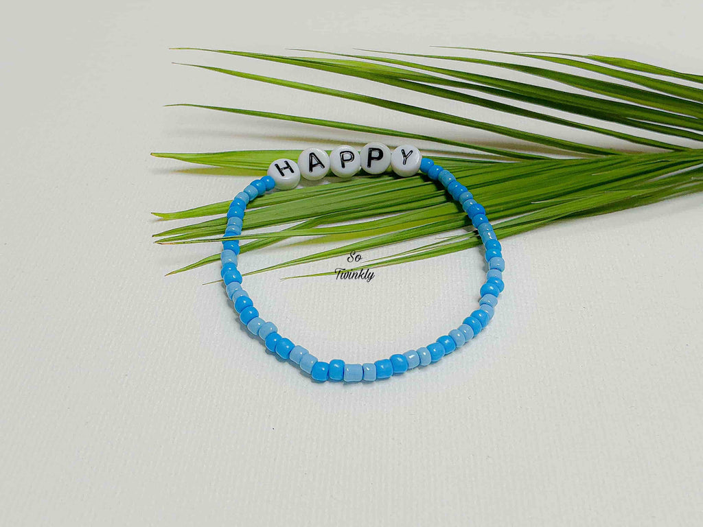 Handmade blue gradient bracelet with acrylic pearls and “Happy” message charm on a soft, minimalist design