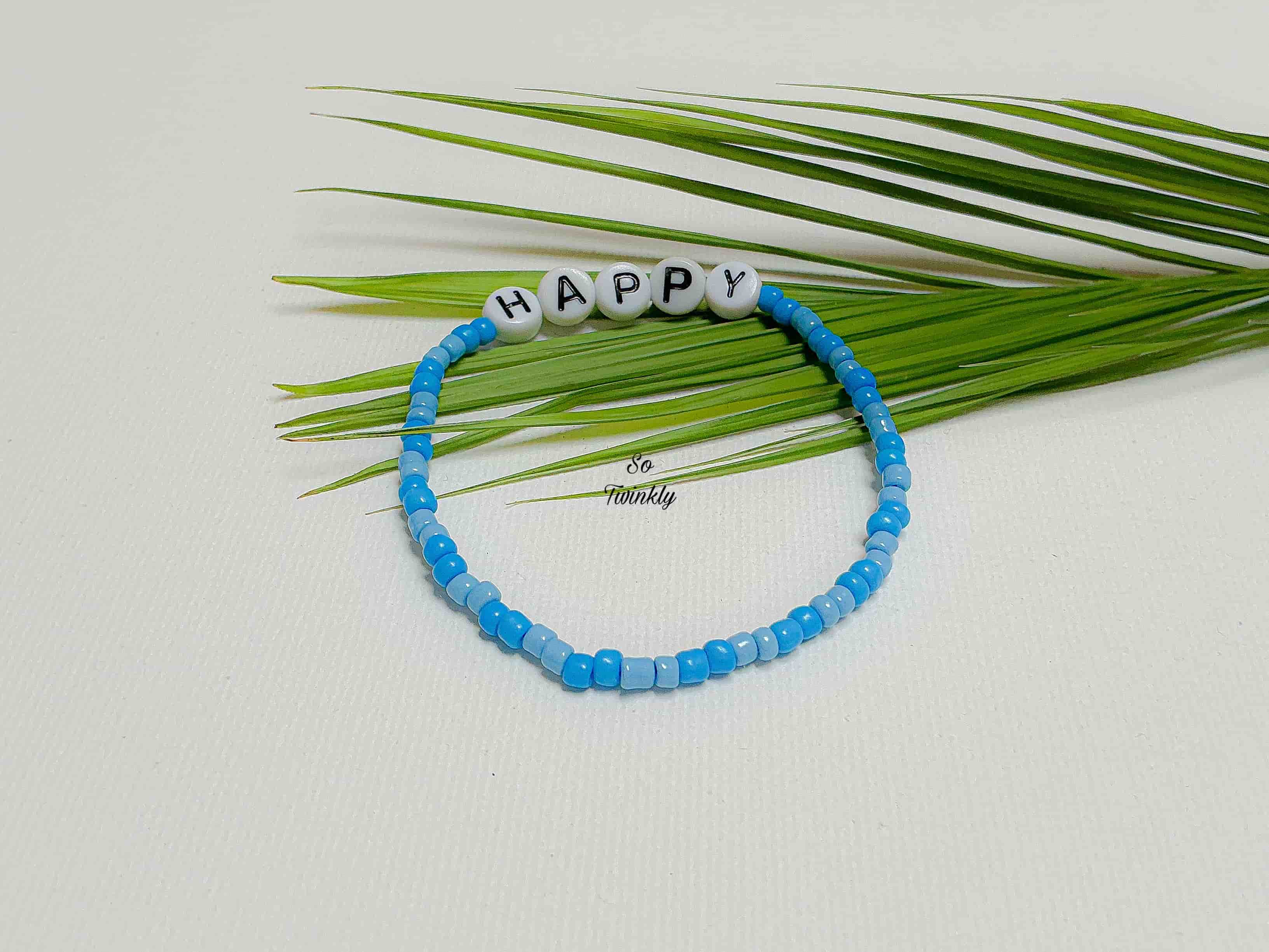 Handmade blue gradient bracelet with acrylic pearls and “Happy” message charm on a soft, minimalist design