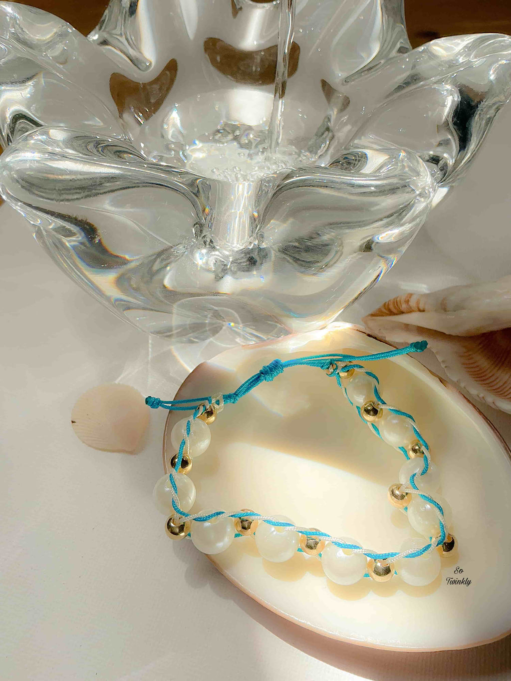 Flat lay of handcrafted bracelet featuring blue and white cords, gold and white pearls, and adjustable nylon cord design