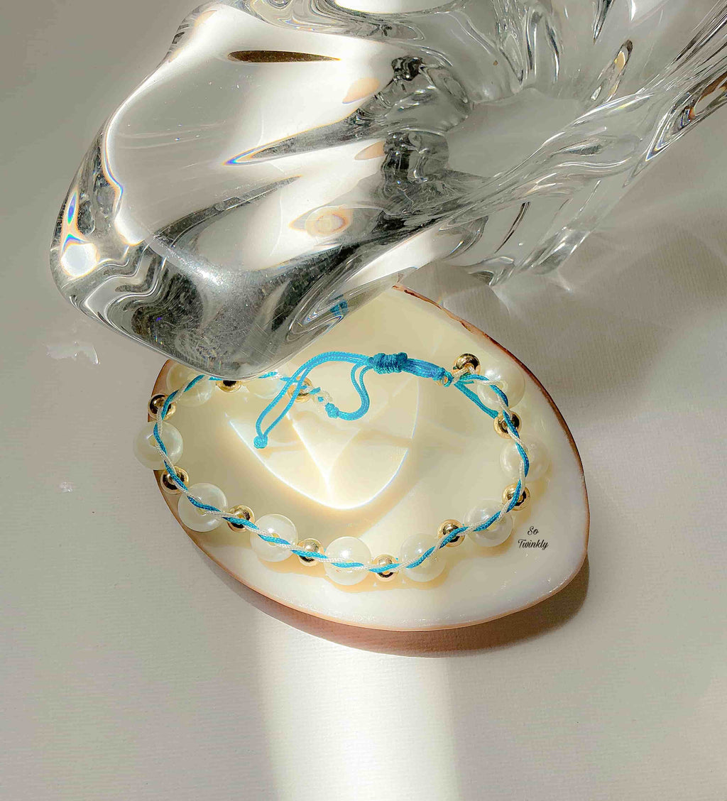 Flat lay of celestial-inspired bracelet with intertwined blue and white cords, gold pearl accents, and adjustable handmade design