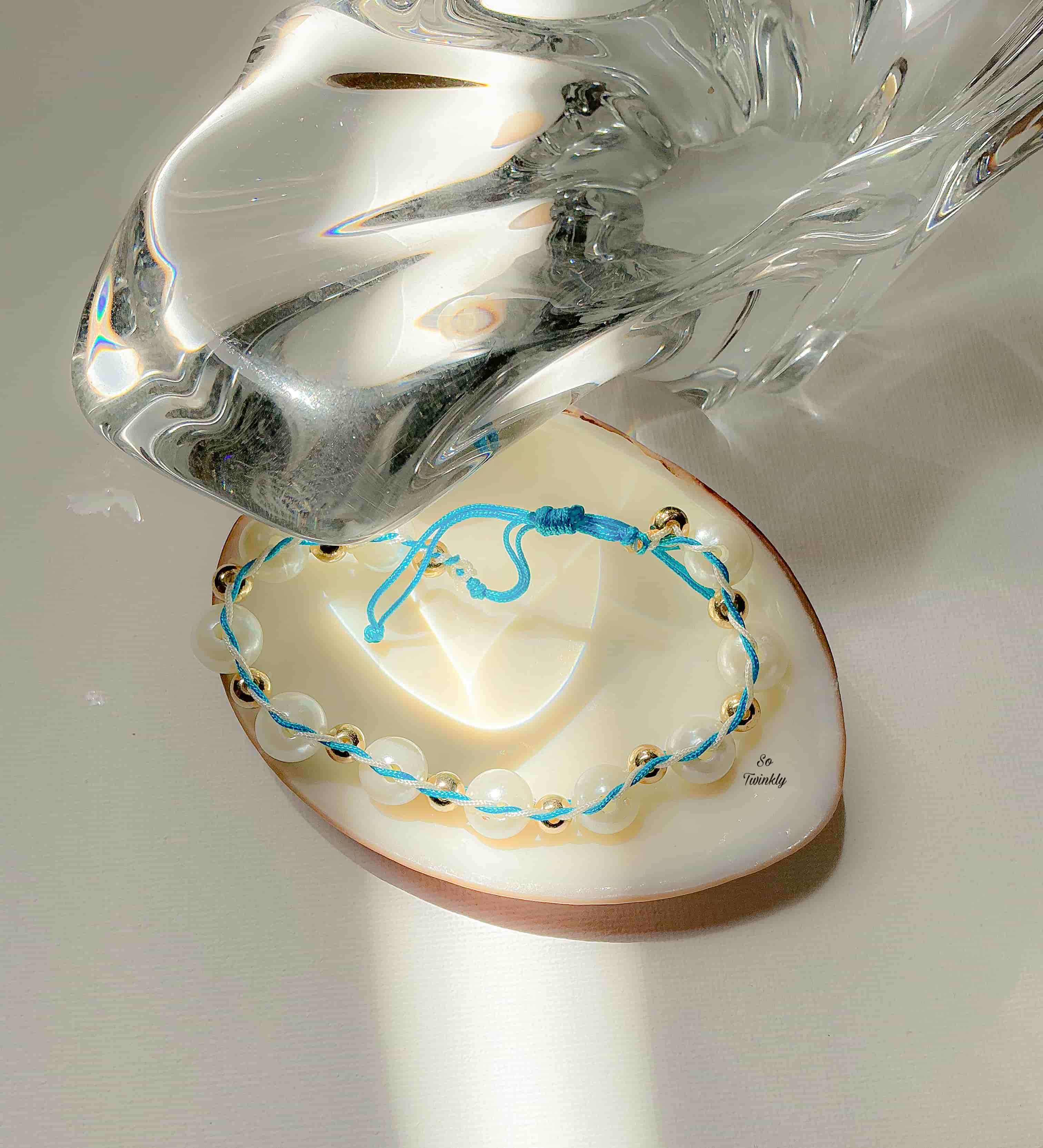 Flat lay of celestial-inspired bracelet with intertwined blue and white cords, gold pearl accents, and adjustable handmade design