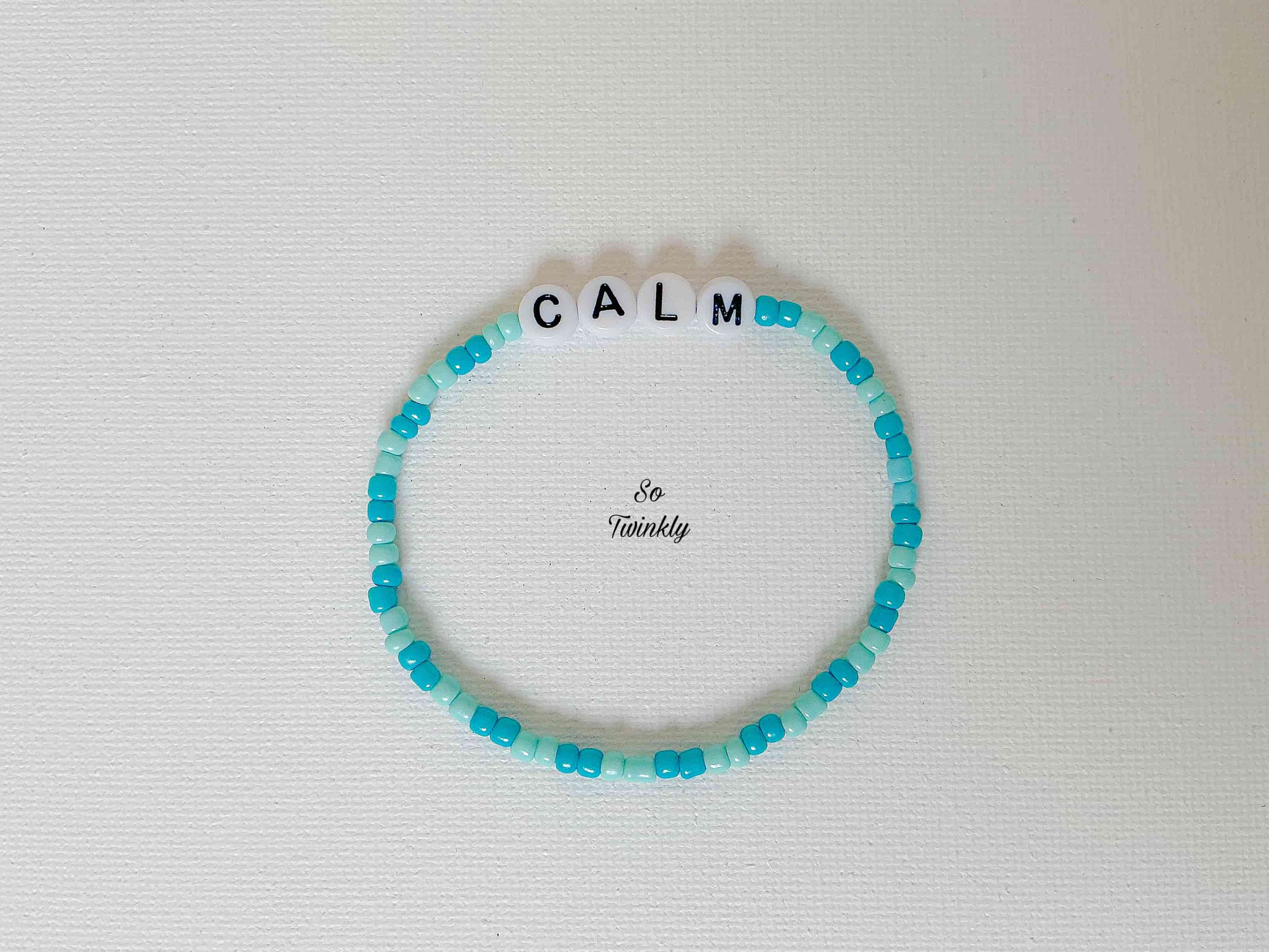 Flat lay of Calm bracelet featuring soft blue acrylic pearls and a minimalist design centered around a peaceful message charm