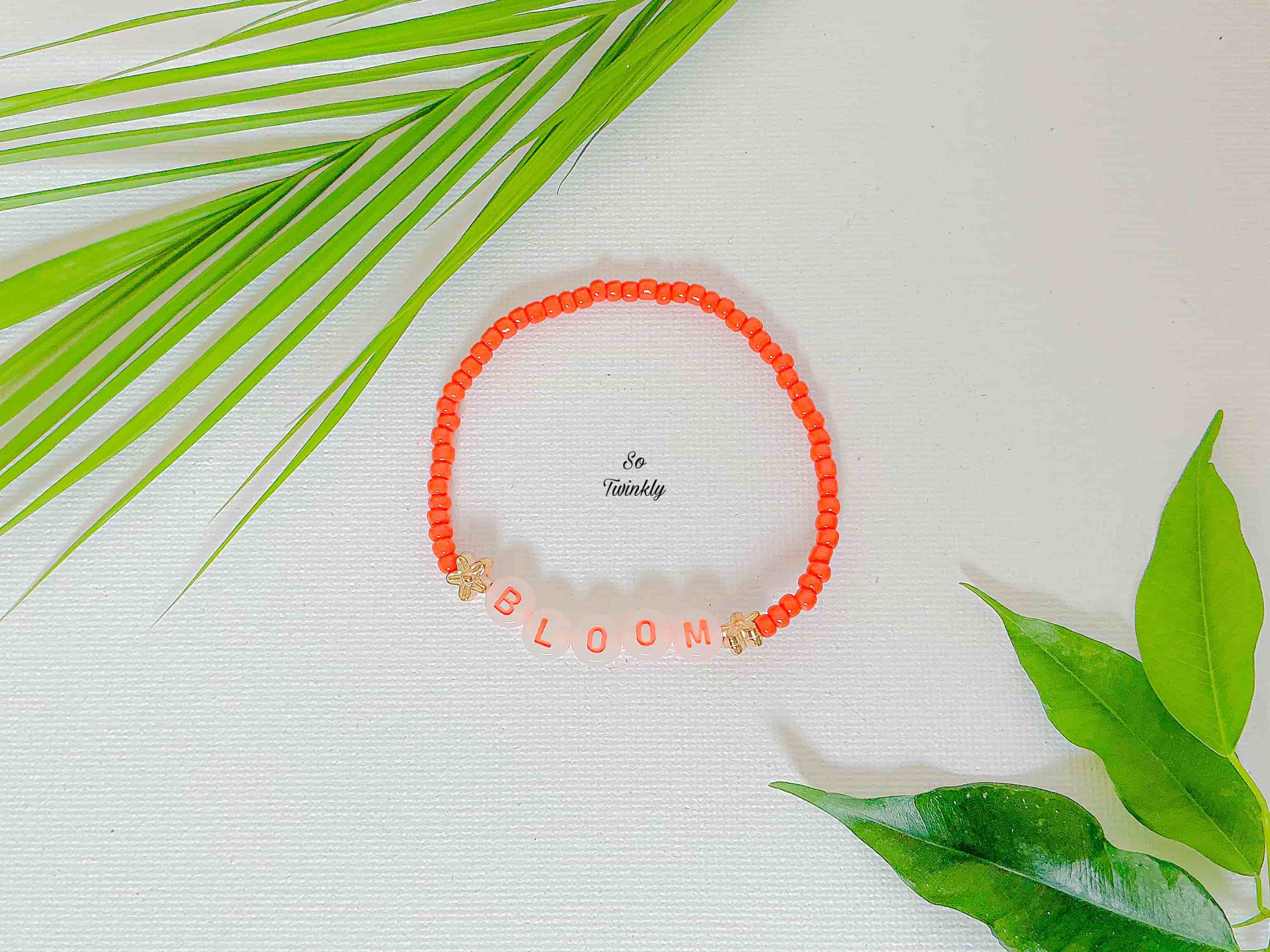 Handmade bracelet with bright neon orange acrylic beads and a bold central message charm that says “BLOOM”