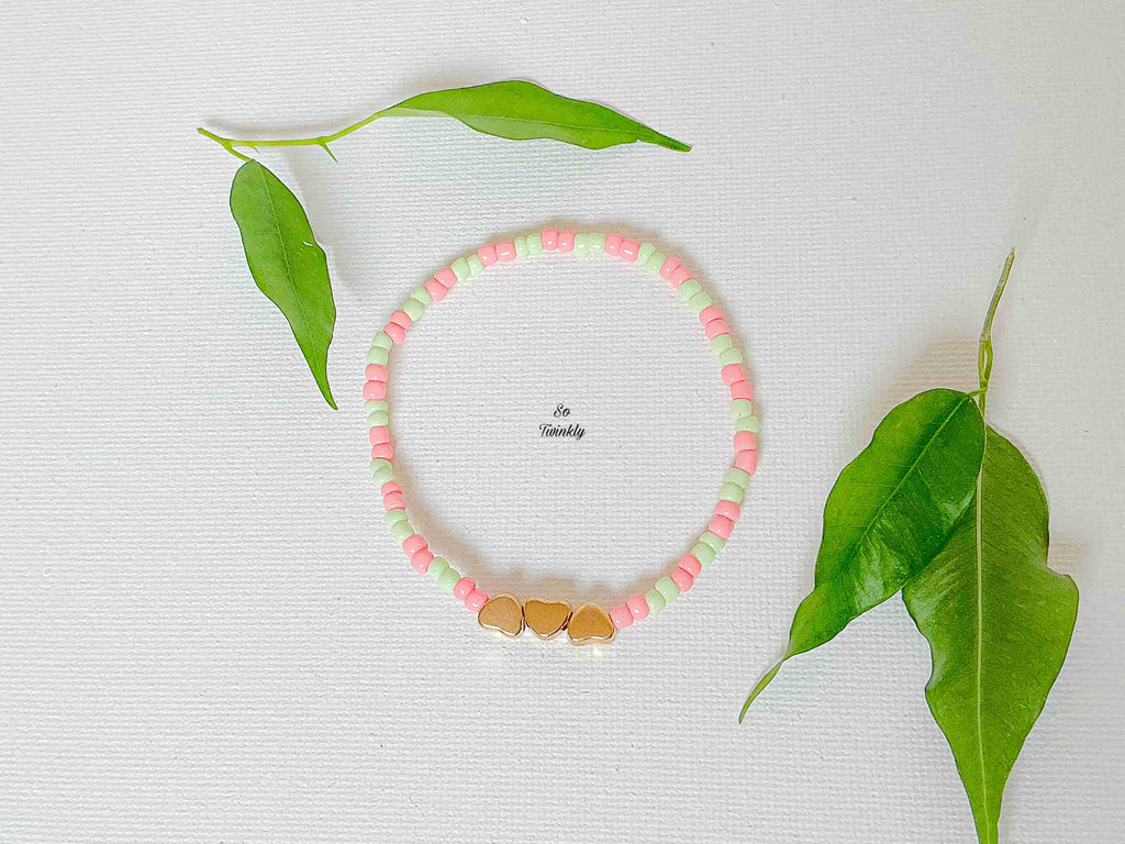 Handmade bracelet with pastel green and pink acrylic beads and three small gold heart charms
