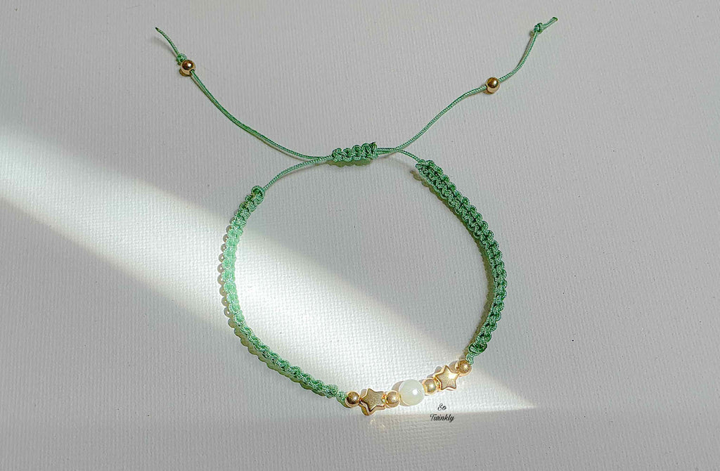 Flat lay of night-sky-inspired bracelet featuring a glowing white pearl, golden star charms, and customizable nylon cord