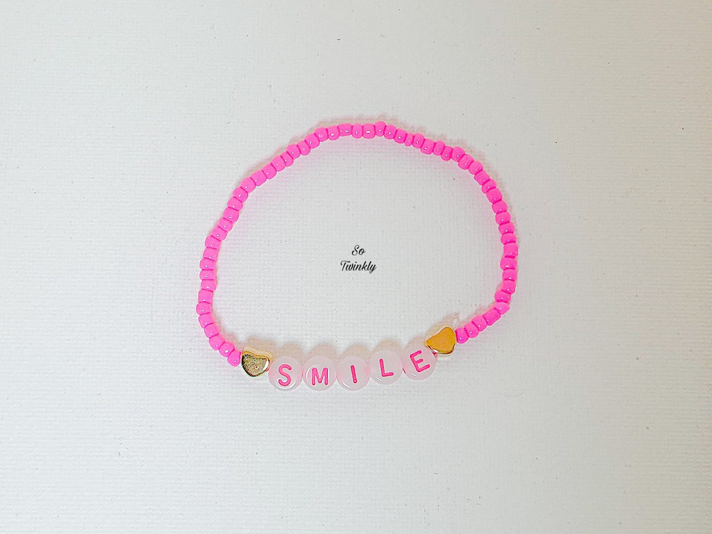 Flat lay of handmade Smile bracelet featuring bright pink acrylic beads and a central message bead that reads “Smile”