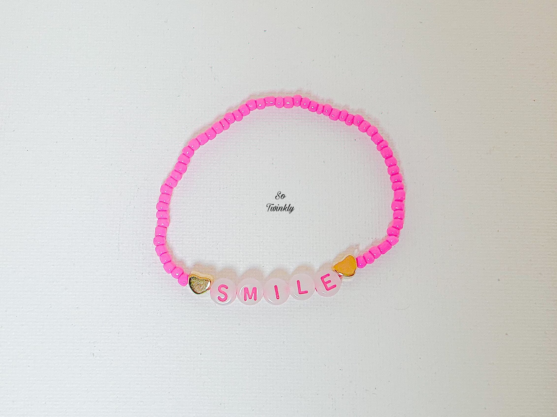 Flat lay of handmade Smile bracelet featuring bright pink acrylic beads and a central message bead that reads “Smile”