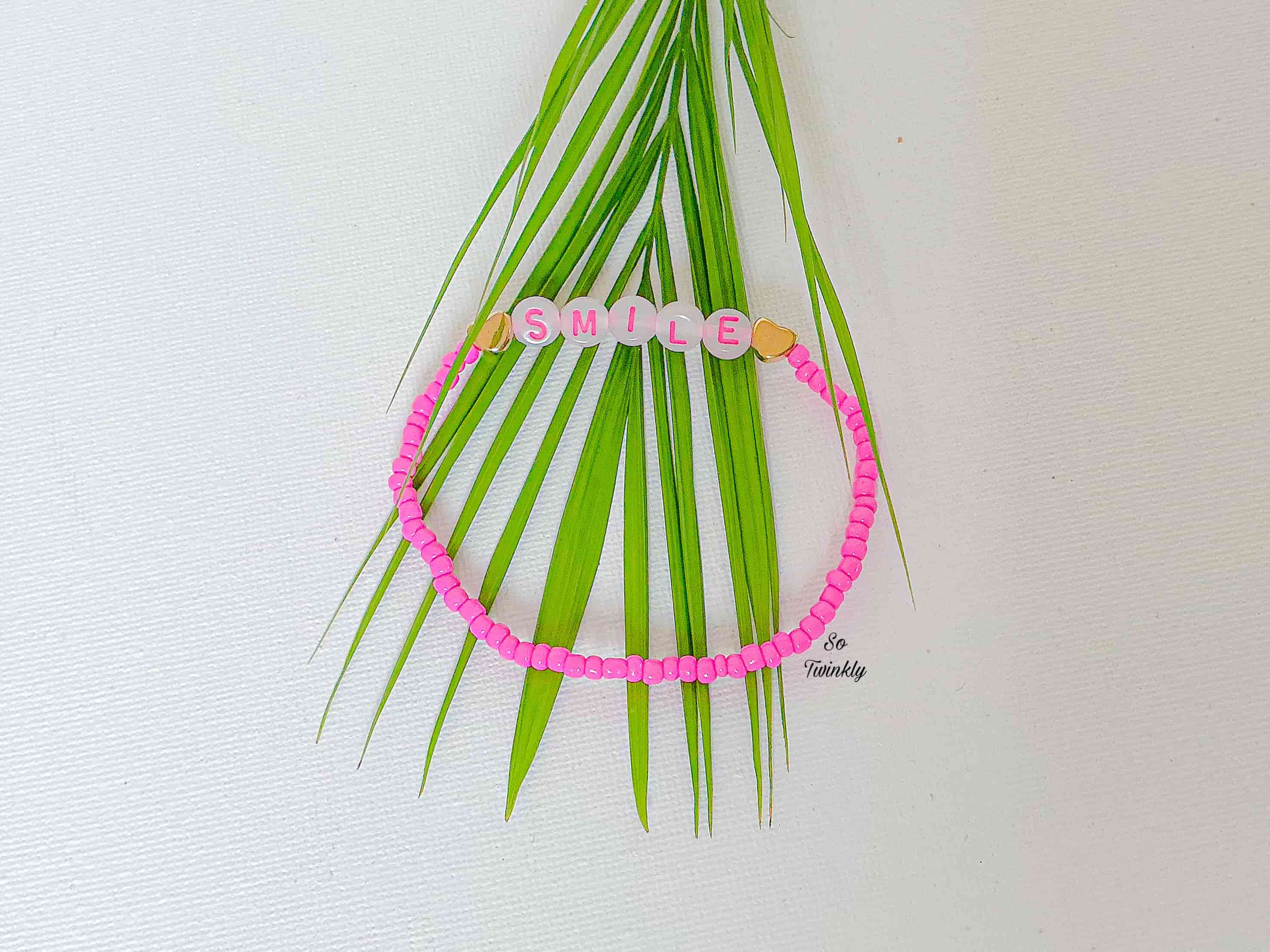 Handmade pink bracelet with acrylic pearls and a cheerful “Smile” message charm in a playful, minimalist design