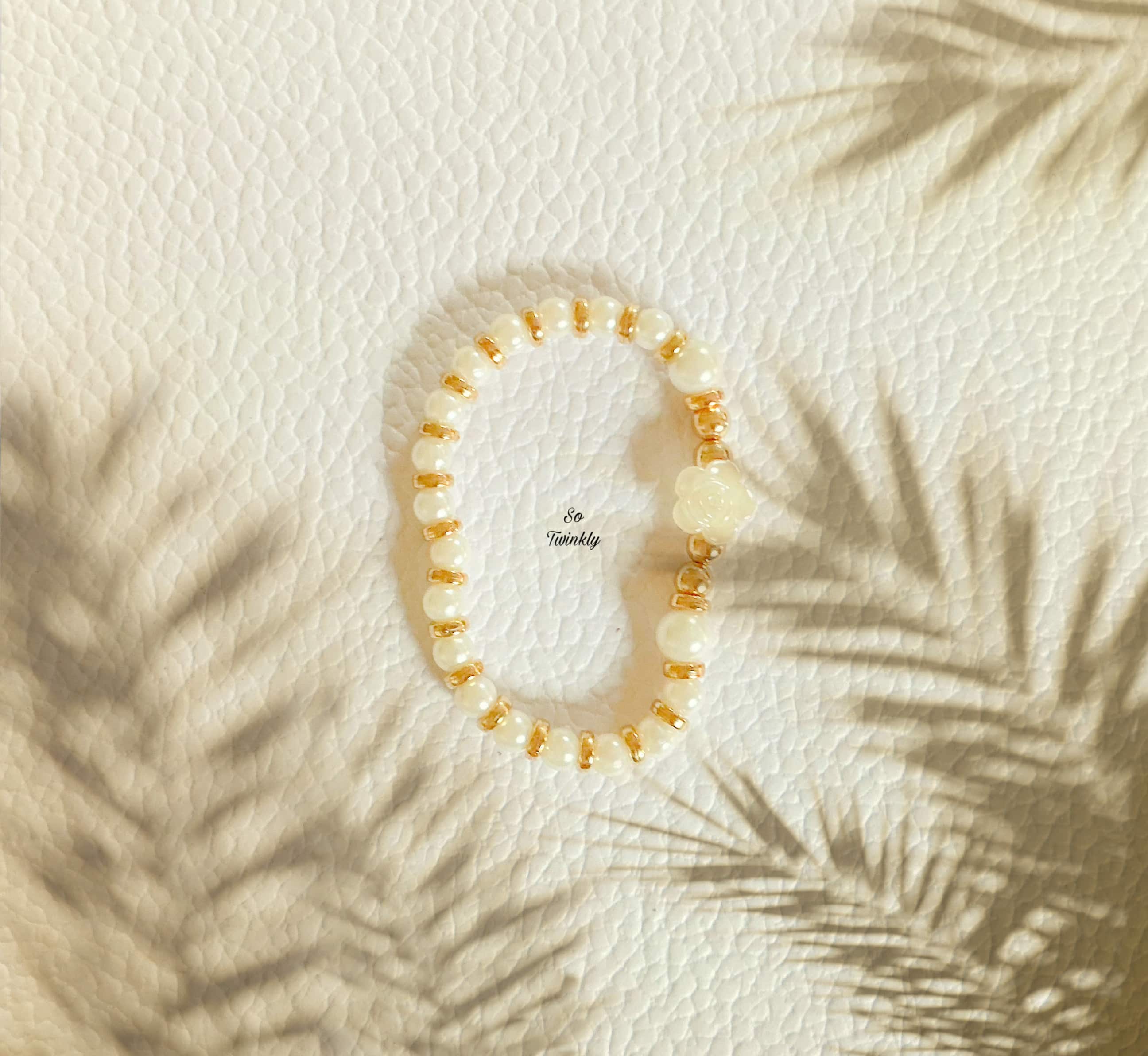 Flat lay of rose charm bracelet featuring white and gold beads in a soft, elegant handcrafted design