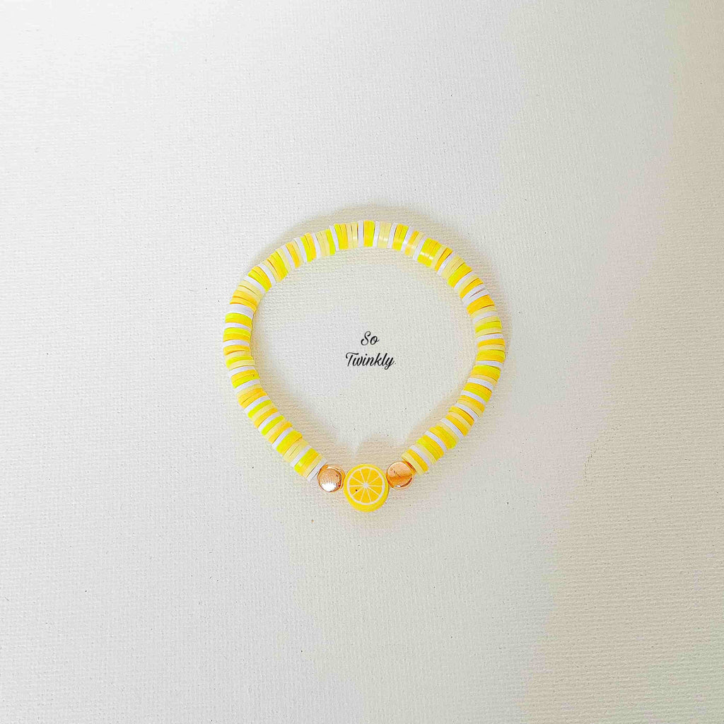 Flat lay of handmade lemon bracelet with gold pearls, white and neon polymer beads